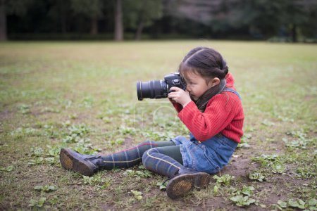 Photo for Asian little girl taking picture with camera outdoors - Royalty Free Image