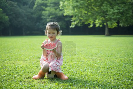 Téléchargez les photos : Mignonne asiatique petite fille manger pastèque dans un parc - en image libre de droit