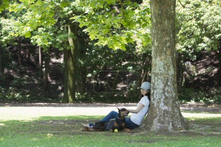 Téléchargez les photos : Femme se détendre avec le Doberman sous un arbre - en image libre de droit