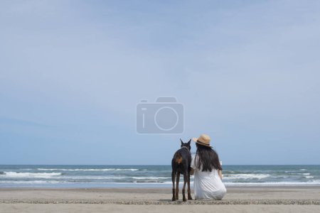 Foto de Mujer relajarse con Doberman en la playa - Imagen libre de derechos