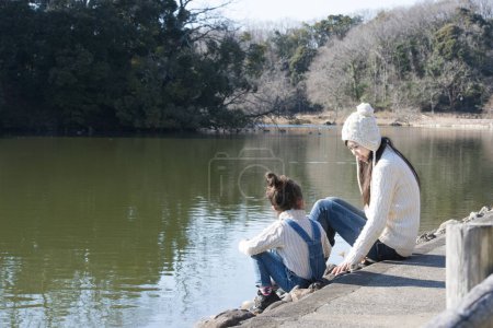 Téléchargez les photos : Mère et fille assises sur le bord de l'étang - en image libre de droit