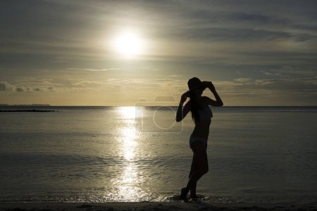 Téléchargez les photos : Silhouette de belle femme relaxante sur la plage du coucher du soleil - en image libre de droit
