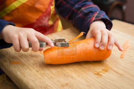 Téléchargez les photos : Les enfants épluchent la carotte de peau - en image libre de droit