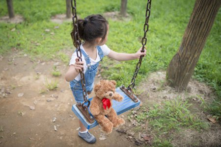 Foto de Lindo poco asiático chica con teddy oso en swing en el parque - Imagen libre de derechos