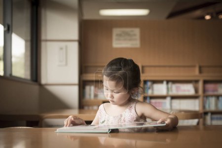 Photo for Asian little girl reading book in library - Royalty Free Image