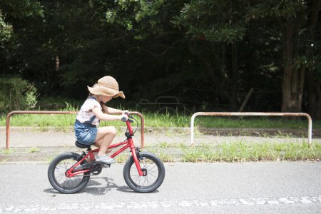 Foto de Lindo poco asiático chica equitación bicicleta en parque - Imagen libre de derechos