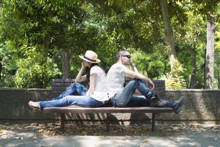 Photo for Couple sit together back to back on bench - Royalty Free Image