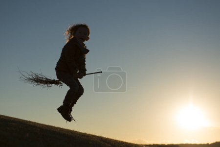 Téléchargez les photos : Une fille avec balai dans le champ au coucher du soleil - en image libre de droit