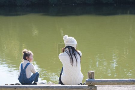 Photo for Mother and daughter sitting on the bank of the pond - Royalty Free Image