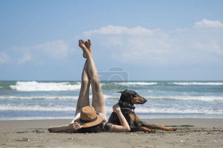 Téléchargez les photos : Femme et Doberman se détendre sur la plage - en image libre de droit