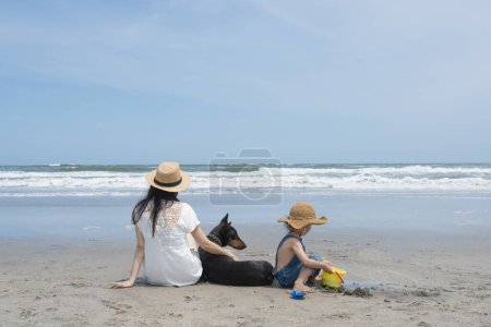 Téléchargez les photos : Mère et enfant et Doberman se détendre sur la plage - en image libre de droit