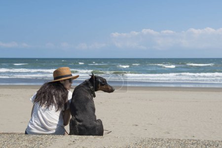 Foto de Mujer y Doberman relajarse en la playa - Imagen libre de derechos