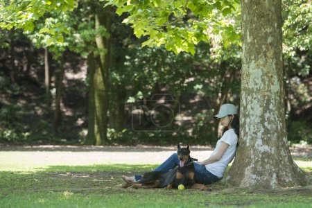 Foto de Mujer relajarse con el Doberman bajo un árbol - Imagen libre de derechos