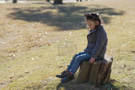 Photo for Little girl in autumn park sitting on stump - Royalty Free Image