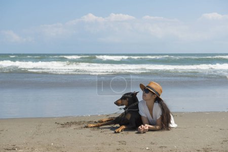 Photo for Woman and Doberman relax on the beach - Royalty Free Image