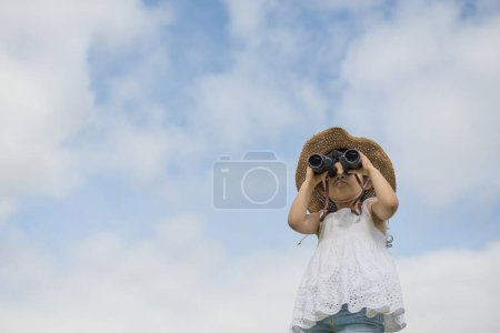 Photo for Cute little asian girl   with binoculars on a background of blue sky - Royalty Free Image