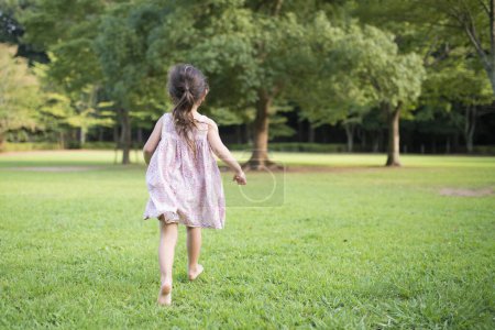 Foto de Lindo poco asiático chica en vestido corriendo en el parque - Imagen libre de derechos