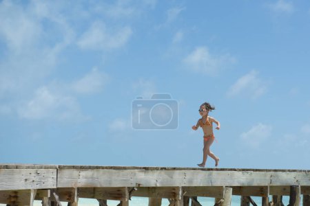 Téléchargez les photos : Fille en bikini courir sur jetée par la mer - en image libre de droit