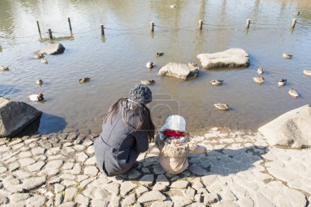 Téléchargez les photos : Mère et fille regardant un oiseau dans un étang - en image libre de droit