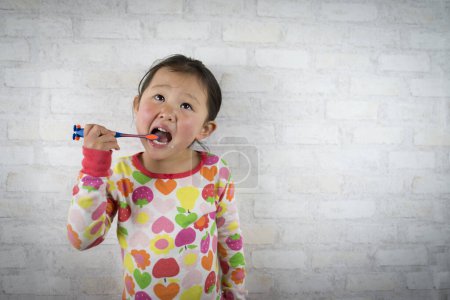 Foto de Lindo poco asiático chica con cepillo de dientes en gris fondo - Imagen libre de derechos