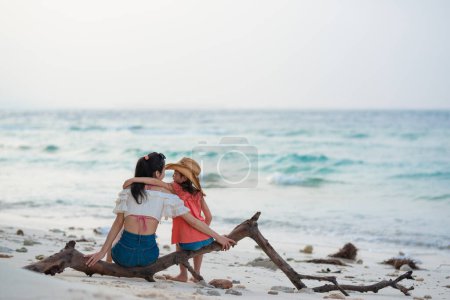 Téléchargez les photos : Mère et fille assises sur du bois flotté sur la plage - en image libre de droit