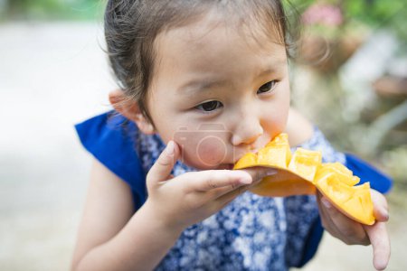 Téléchargez les photos : Bonne petite fille mangeant de la mangue - en image libre de droit