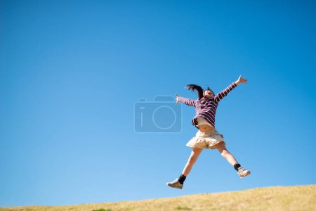 Téléchargez les photos : Mignonne petite fille asiatique sautant dans l'air contre ciel bleu - en image libre de droit