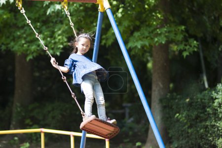 Téléchargez les photos : Fille jouer sur swing dans une aire de jeux. - en image libre de droit
