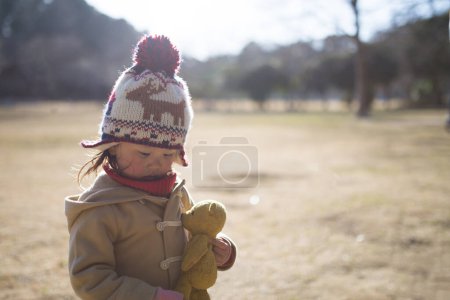 Téléchargez les photos : Petite fille jouer avec ours en peluche par une journée ensoleillée dans le parc - en image libre de droit