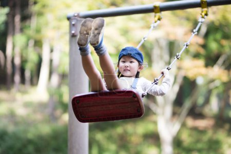 Téléchargez les photos : Belle petite fille asiatique sur swing dans une aire de jeux dans le parc - en image libre de droit