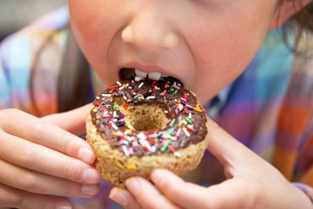 Foto de Niño comiendo colorido donut de chocolate - Imagen libre de derechos