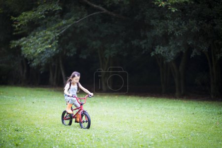 Foto de Lindo poco asiático chica equitación bicicleta en prado - Imagen libre de derechos