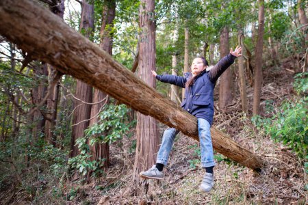 Téléchargez les photos : Mignonne petite fille asiatique sur tronc dans forêt - en image libre de droit