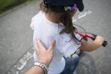 Téléchargez les photos : Main poussant le dos d'un enfant en vélo - en image libre de droit
