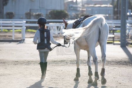 Téléchargez les photos : Mignonne petite fille asiatique avec son cheval sur une piste dans l'écurie - en image libre de droit