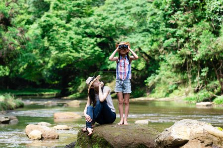 Photo for Mother and daughter using binoculars on mountain stream rocks - Royalty Free Image