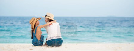 Foto de Madre e hija sentadas en la playa de arena y hablando - Imagen libre de derechos