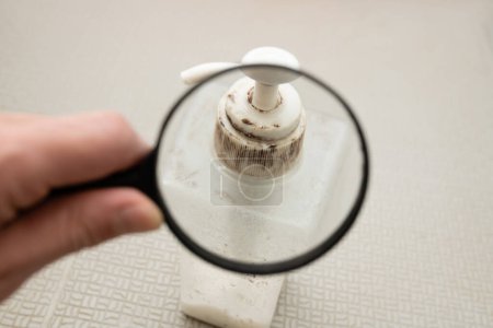 Foto de Mira el molde en el recipiente de champú con una lupa - Imagen libre de derechos