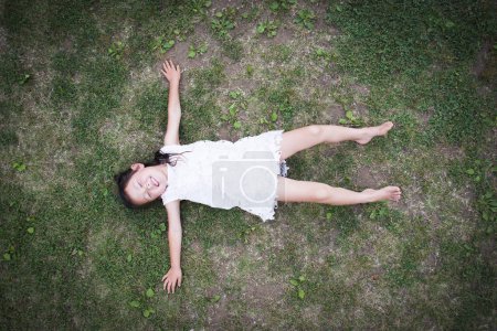 Téléchargez les photos : Bonne petite fille se détendre sur la pelouse - en image libre de droit