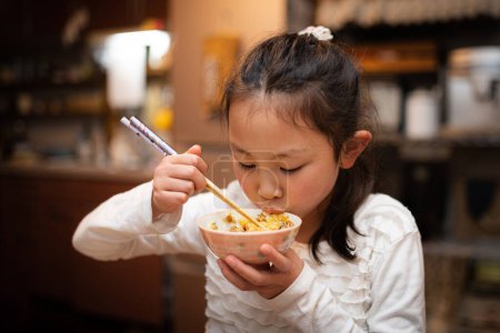 Téléchargez les photos : Une fille mangeant du riz avec des baguettes et un bol - en image libre de droit