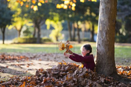 Little girl playing with fallen leaves