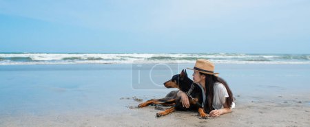 Téléchargez les photos : Femme relax avec Doberman sur la plage - en image libre de droit