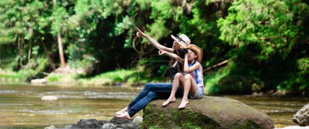 Photo for Mother and daughter using binoculars on mountain stream rocks - Royalty Free Image