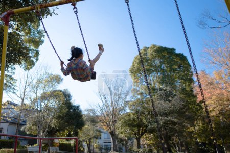 Téléchargez les photos : Mignonne petite fille asiatique sur swing sur une aire de jeux dans le parc - en image libre de droit