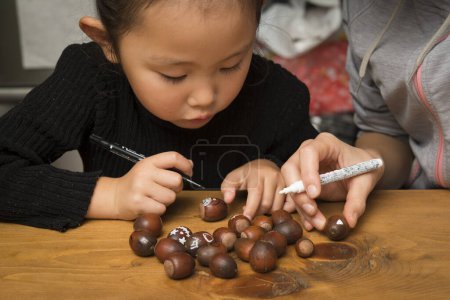 Photo for Mother and daughter drawing a pattern on acorns - Royalty Free Image