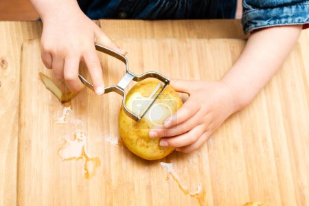 Téléchargez les photos : Mains d'un enfant épluchant une pomme de terre - en image libre de droit