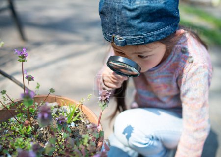 Téléchargez les photos : Mignonne petite fille à la recherche de fleurs avec loupe - en image libre de droit