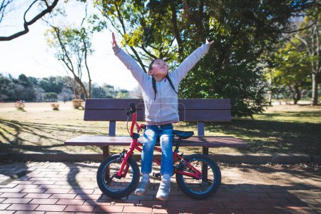 Foto de Chica feliz con bicicleta en un bosque sentado en el banco - Imagen libre de derechos