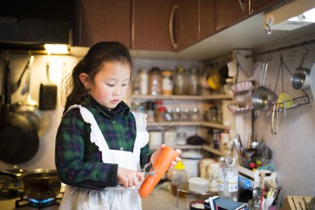 Téléchargez les photos : Petite fille peler la carotte sur la cuisine - en image libre de droit