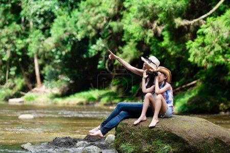 Foto de Madre e hija usando prismáticos en rocas del arroyo de montaña - Imagen libre de derechos